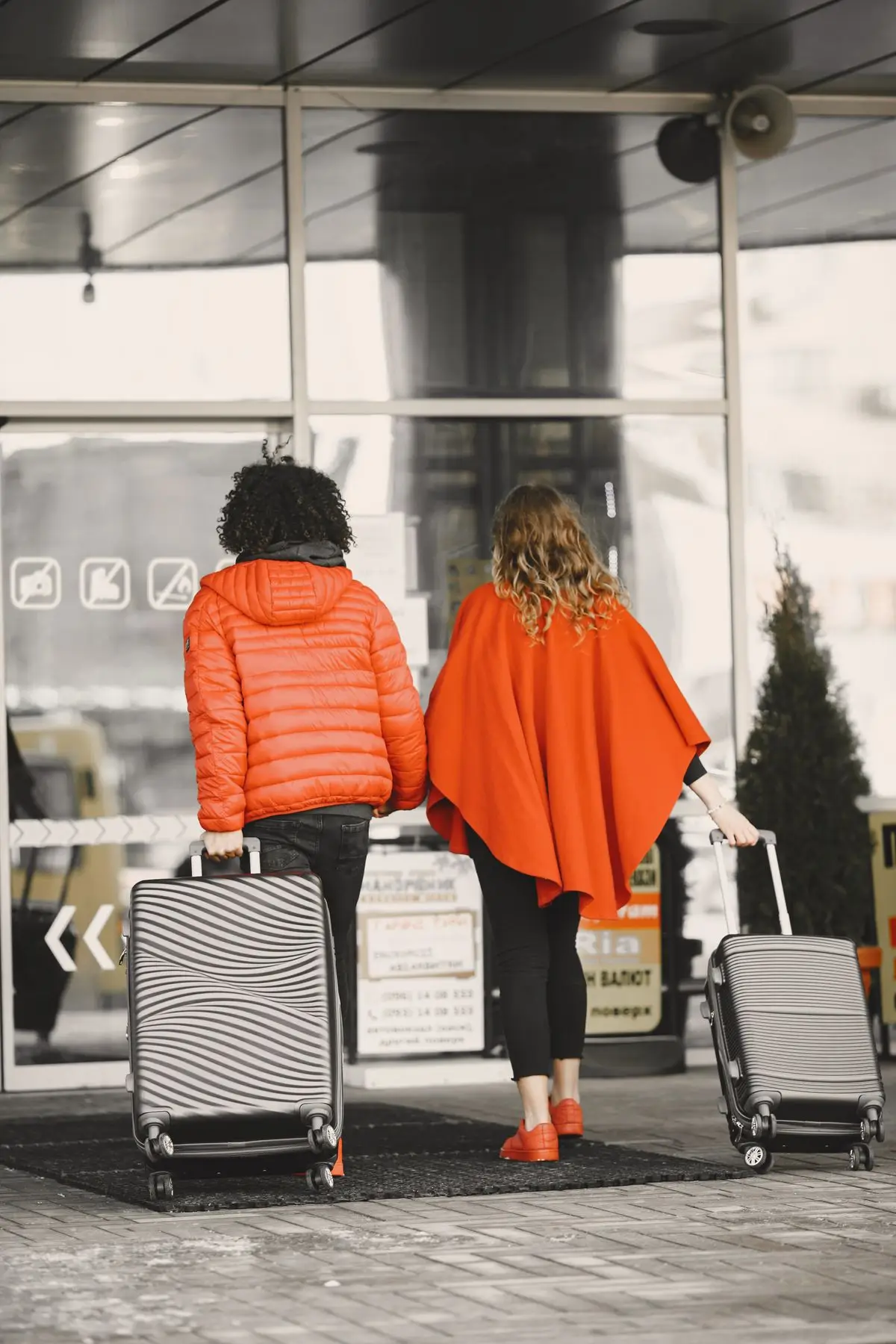 Two travellers with suitcases at an airport entrance