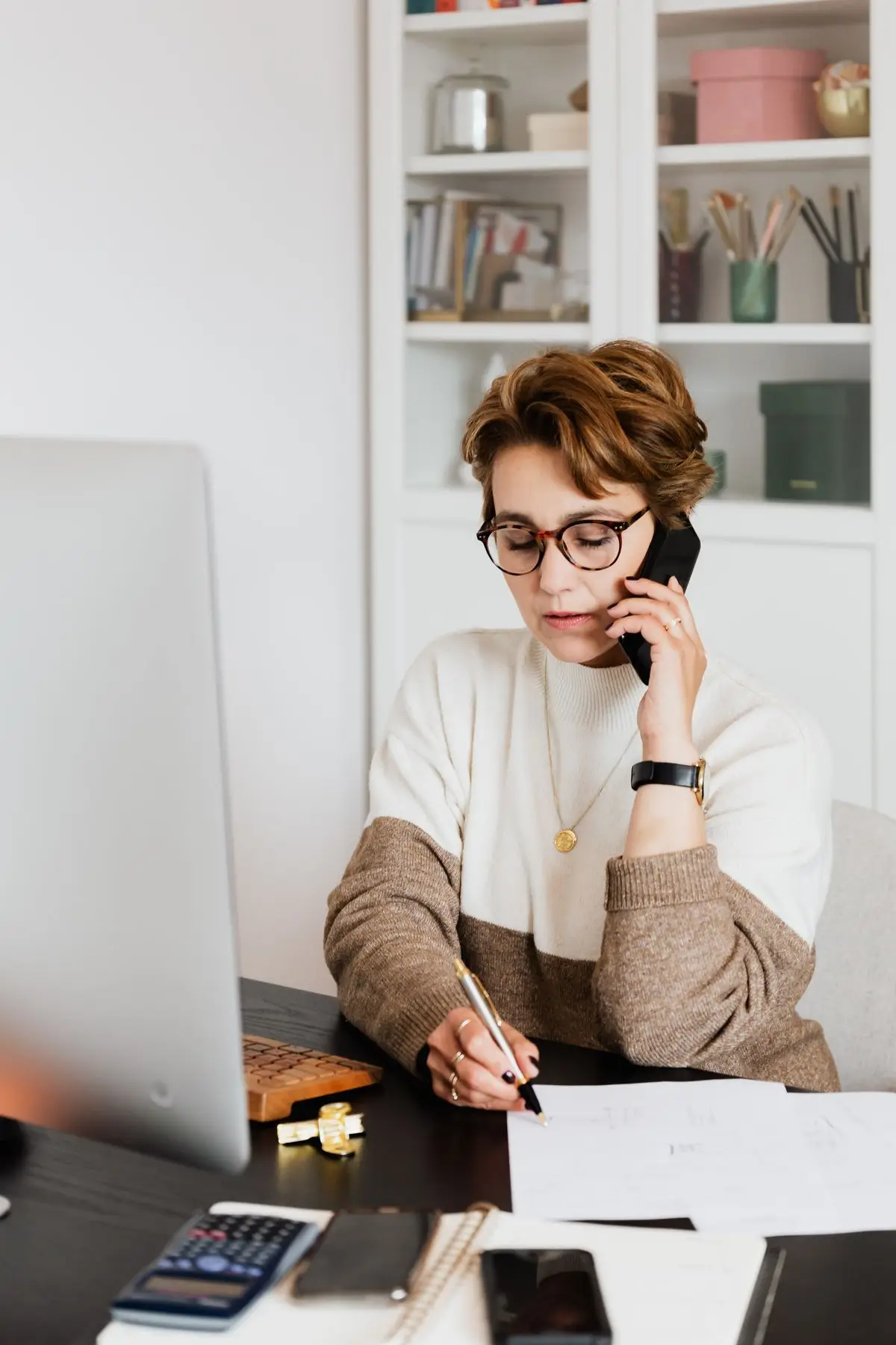 A woman taking notes on a call at her desk